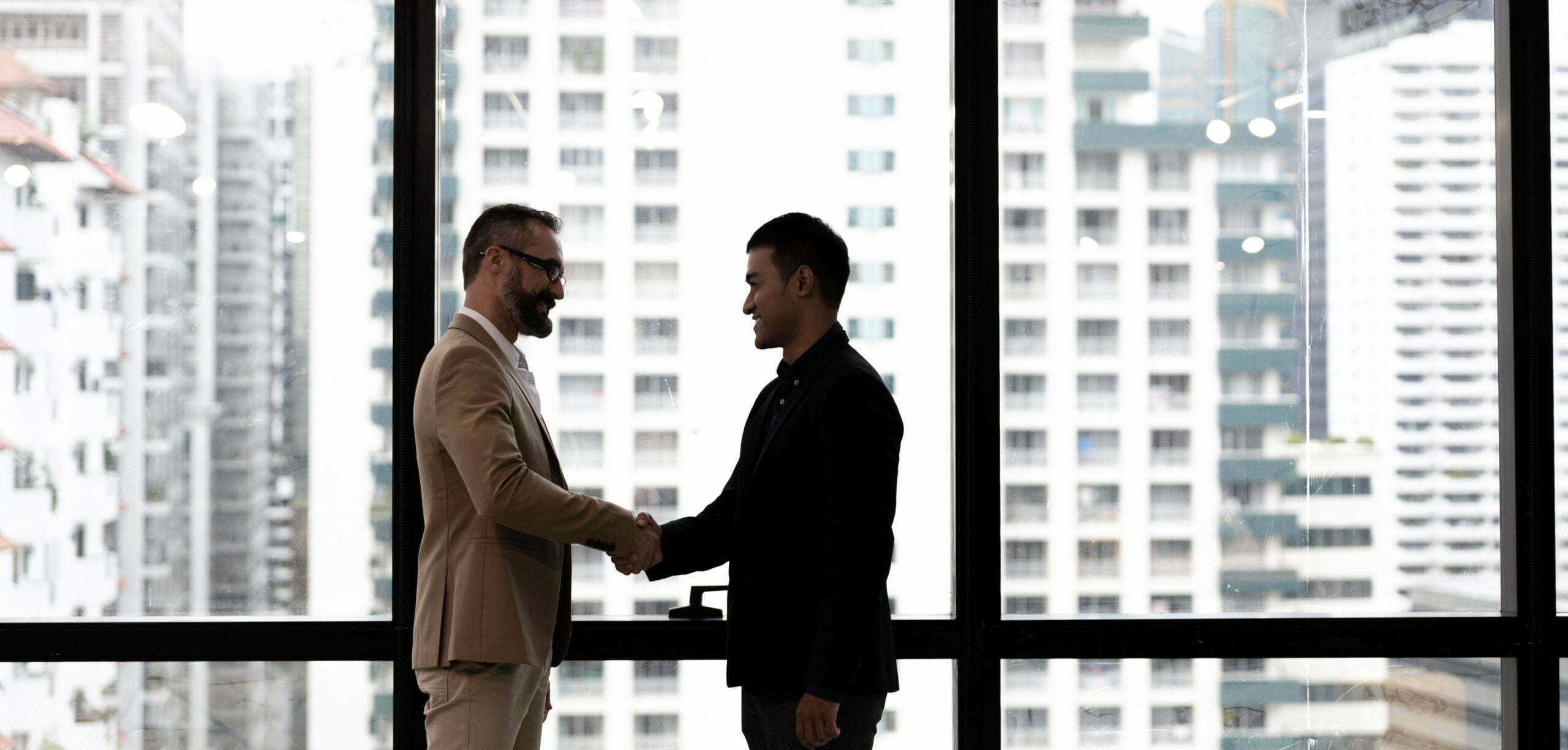 a man shaking hands with a man in a suit in front of a window
